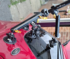 Camera tripod mounted on a red vehicle with a cloudy sky background