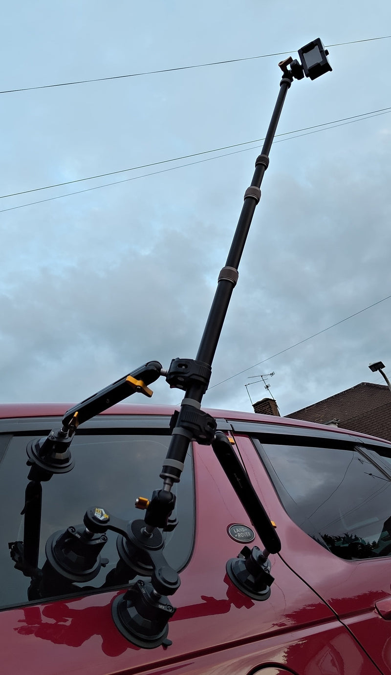 Camera tripod mounted on a red vehicle with a cloudy sky background