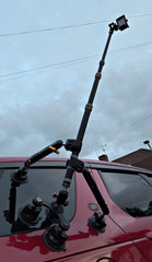 Camera tripod mounted on a red vehicle with a cloudy sky background