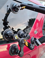 Camera tripod mounted on a red vehicle with a cloudy sky background